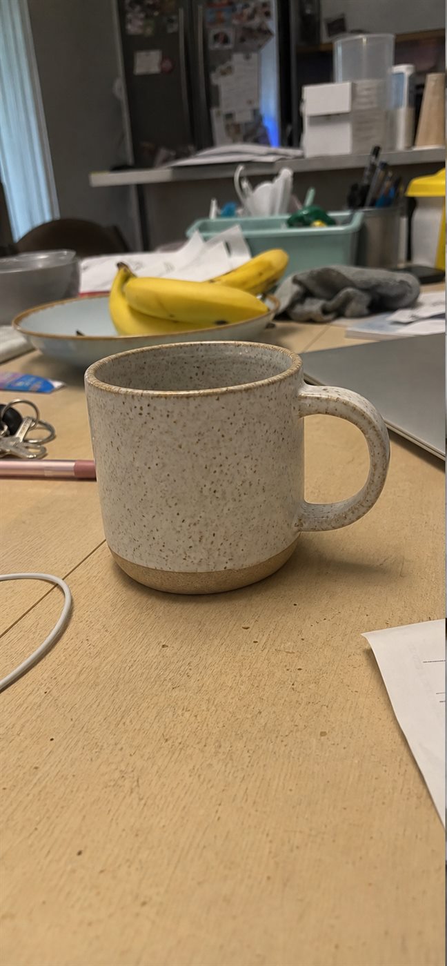 Crummy iPhone reference photo of a handmade ceramic mug on a cluttered home table